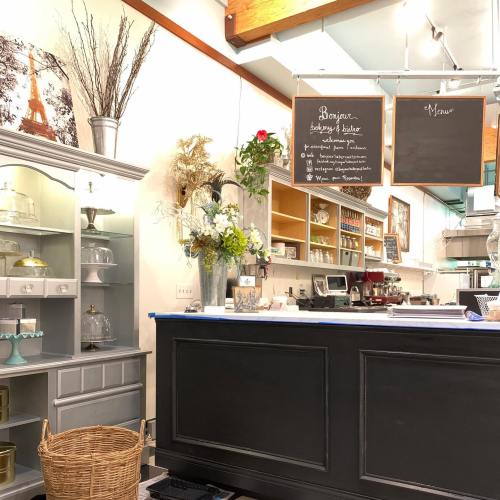 Cozy café interior featuring a counter, display shelves, and decorative plants, with chalkboards for menu and greetings.
