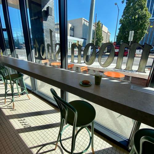 A bright café interior with a long counter, a drink, and a pastry, featuring large windows and modern seating.