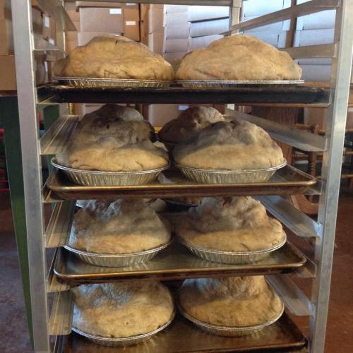 A rack of freshly baked, large round loaves of bread in metal pie pans, stacked in a bakery.