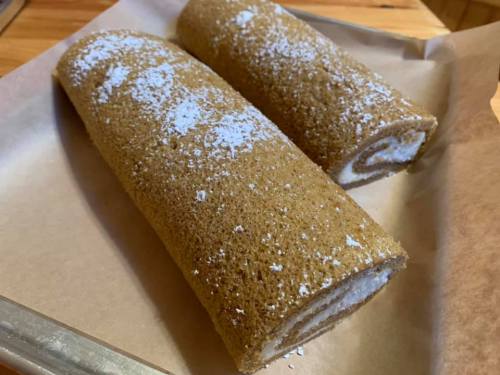 Two rolled sponge cakes dusted with powdered sugar, resting on parchment paper.