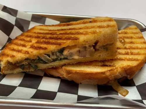 Grilled sandwich with golden-brown crust, filled with greens and melted cheese, served on a checkered paper.