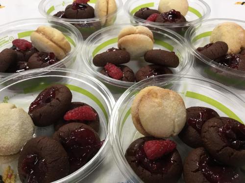 Six clear containers filled with chocolate and vanilla cookies topped with raspberry jam and fresh raspberries.