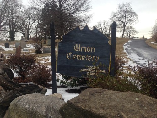 Sign for Union Cemetery, with a gravel path and gravestones visible in the background, surrounded by bare trees.