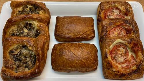 A platter of assorted pastries, including mushroom and tomato-filled puff pastries, on a white serving tray.