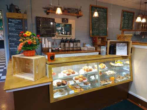 A cozy café counter displaying a variety of pastries and desserts, with chalkboard menus and a flower arrangement.