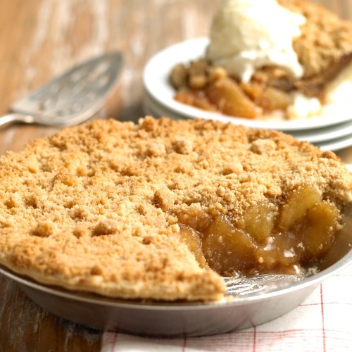 A freshly baked apple pie with a crumbly topping, served with a slice and a scoop of vanilla ice cream on the side.