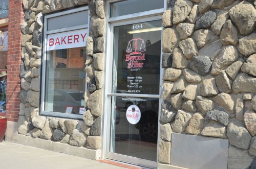 Exterior view of a bakery with a stone facade and a glass door displaying business hours and contact information.