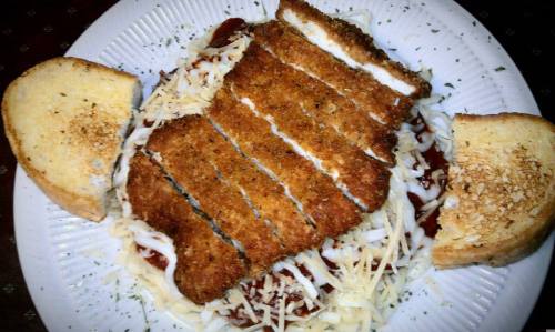 A plate of crispy fried chicken on a bed of pasta with cheese and sauce, accompanied by two slices of toasted bread.