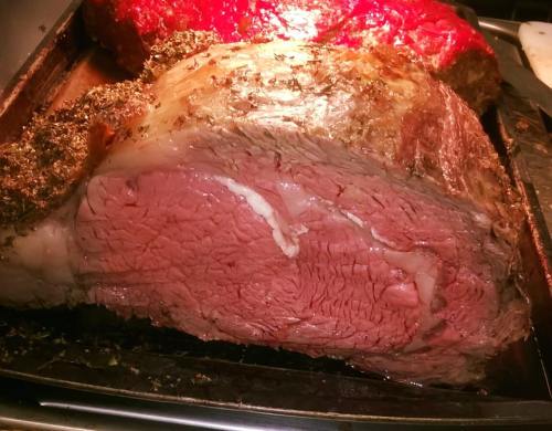 A large, cooked roast beef with a seasoned crust, showcasing a juicy, pink interior on a roasting pan.