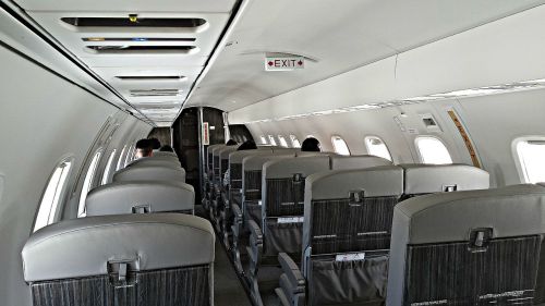 Interior of an airplane showing empty rows of seats and an exit sign above.