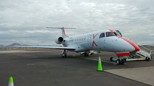 A sleek white and red private jet parked on an airport tarmac under a cloudy sky.