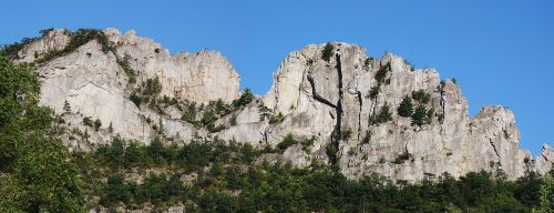 A rugged mountain range with steep cliffs and patches of greenery under a clear blue sky.