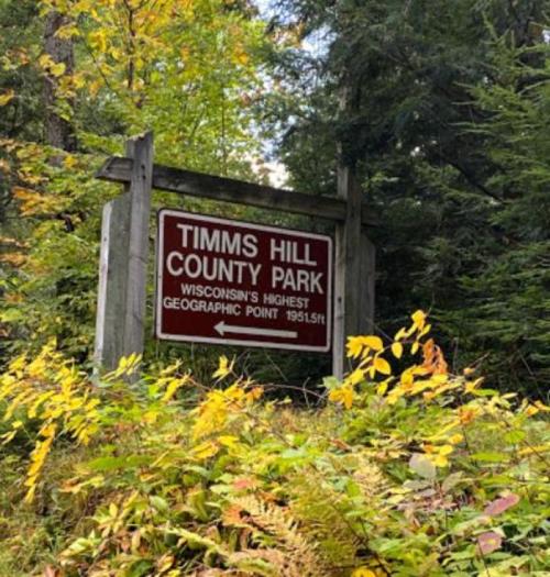 Sign for Timms Hill County Park, noting it as Wisconsin's highest geographic point at 1951.5 ft, surrounded by greenery.
