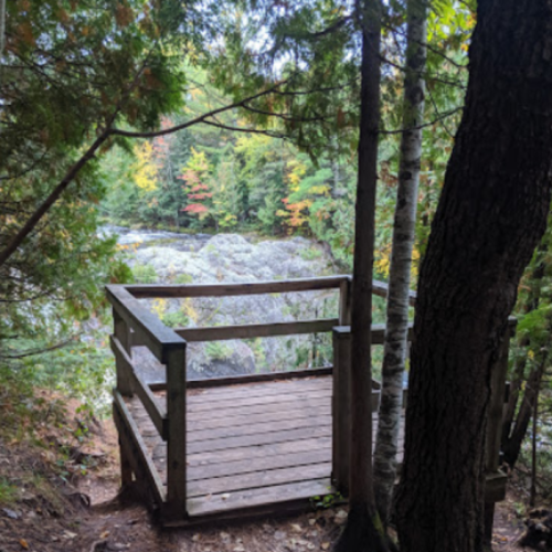 A wooden viewing platform surrounded by trees, overlooking a rocky landscape with autumn foliage.