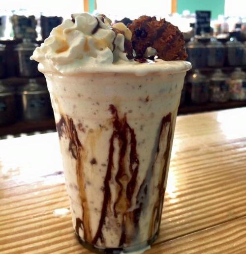A creamy milkshake topped with whipped cream, chocolate drizzle, and a cookie on the rim, served in a clear cup.