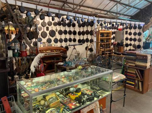 A vintage shop interior filled with hanging cast iron pans, antique items, and a display case of collectibles.
