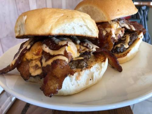 Two hearty burgers stacked with bacon and sauce, served on soft buns on a white plate.