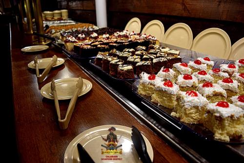 A dessert buffet featuring various cakes and pastries, topped with cherries and whipped cream, on a wooden table.
