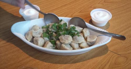 A dish of dumplings topped with chopped herbs, served with two small cups of sour cream on a wooden table.