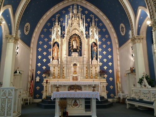 Interior of a church featuring an ornate altar with statues, blue walls, and decorative arches.