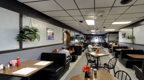 A cozy restaurant interior with booths, tables, and plants, featuring diners enjoying their meals in a relaxed atmosphere.