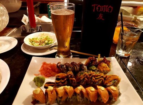 A plate of sushi rolls with ginger and wasabi, a salad, a beer, and a menu in a restaurant setting.