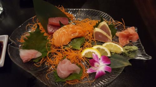 A beautifully arranged sushi platter featuring various sashimi, garnished with lemon, wasabi, and an orchid flower.