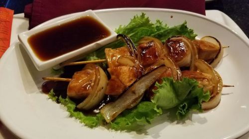 Grilled chicken skewers with onions on a bed of lettuce, served with a side of dipping sauce.