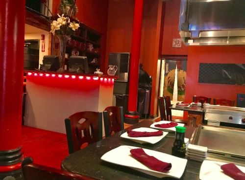 Interior of a restaurant featuring red pillars, dark wooden tables, and a grill station with a vibrant atmosphere.