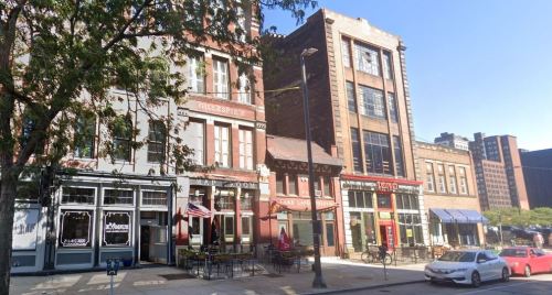 Historic buildings line a city street, featuring cafes and shops with outdoor seating and American flags.