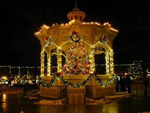 A beautifully lit gazebo adorned with Christmas decorations and a tree, surrounded by festive lights at night.