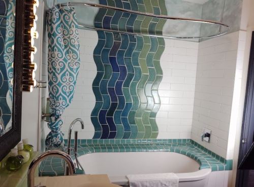 A modern bathroom featuring a curved glass shower, colorful tile accents in blue and green, and a white bathtub.