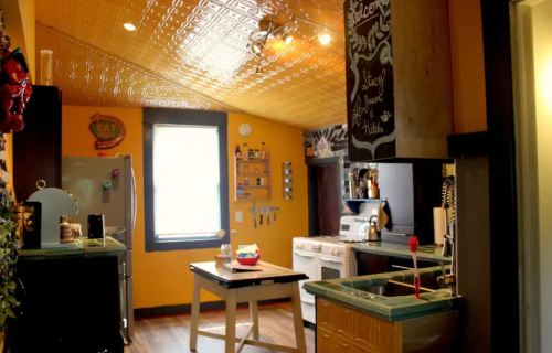 Bright kitchen with yellow walls, vintage decor, a central table, and modern appliances. Natural light from a window.