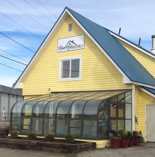 A yellow bistro building with a blue roof and a glass-enclosed patio, featuring a sign that reads "Blue Roof Bistro."