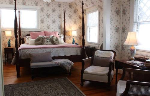 Cozy bedroom with floral wallpaper, a four-poster bed, armchairs, and warm lighting.