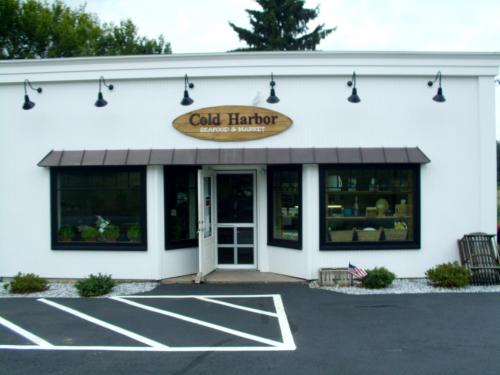 Exterior of Cold Harbor Seafood & Market, featuring a white building with a sign and large windows.