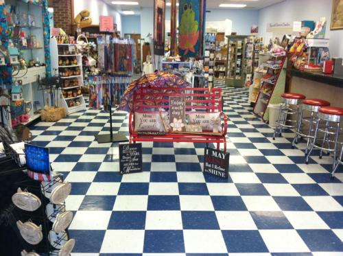 A colorful gift shop interior with a checkered floor, display shelves, and a red bench with decorative signs.