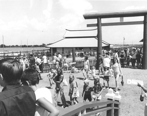 A busy outdoor scene with a crowd of people, including children, near a large structure and a traditional archway.