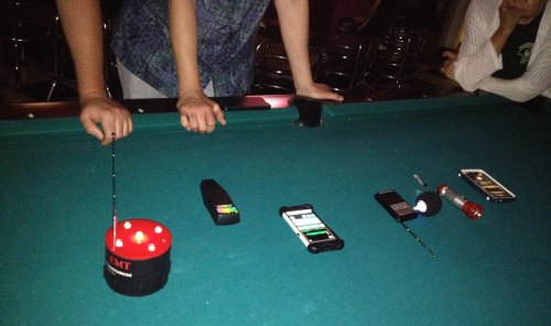 Two hands hover over a pool table with various devices and a red light on the green felt surface.