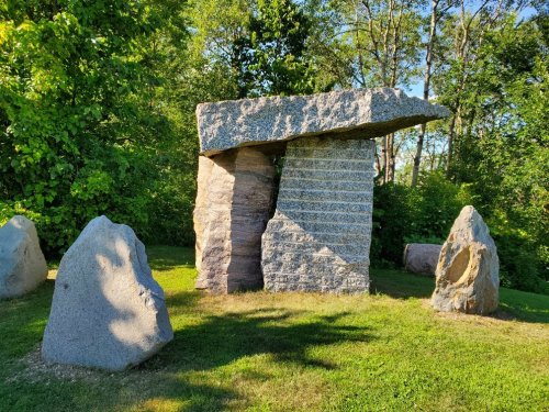 A large stone structure resembling a dolmen, surrounded by smaller rocks and lush greenery.