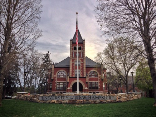 Historic building of the University of New Hampshire, featuring a flagpole and surrounded by trees and grass.