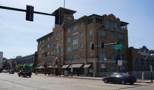 Historic Hotel Baker building on a sunny day, with cars passing by and traffic lights in view.