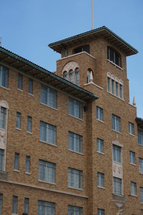 Historic brick building with decorative elements and a tower, set against a clear blue sky.