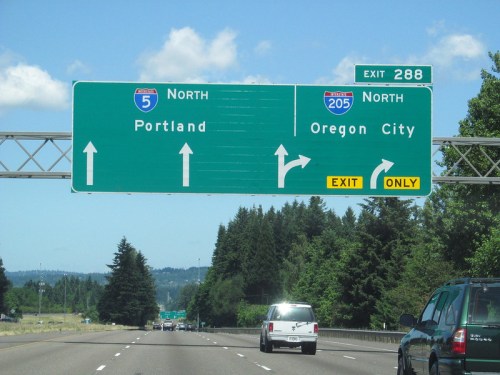 Highway sign indicating directions to Portland and Oregon City, with an exit for I-205 North. Clear blue sky above.