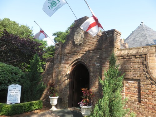 Entrance to the Elizabethan Gardens, featuring brick architecture, flags, and lush greenery.