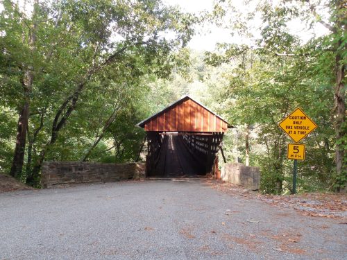 A wooden covered bridge surrounded by trees, with a caution sign for one vehicle at a time and a speed limit of 5 MPH.