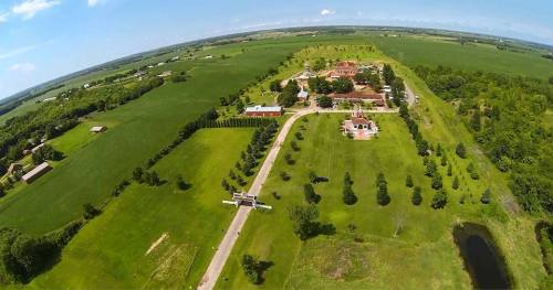 Aerial view of a sprawling green landscape with buildings, trees, and a winding road in a rural setting.