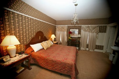 Cozy bedroom with floral wallpaper, a large bed, elegant curtains, and warm lighting from bedside lamps.