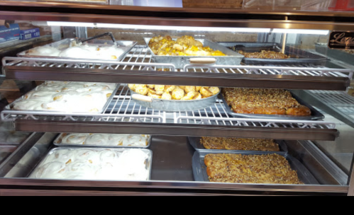 A display case filled with various baked goods, including pastries, cakes, and desserts on metal trays.