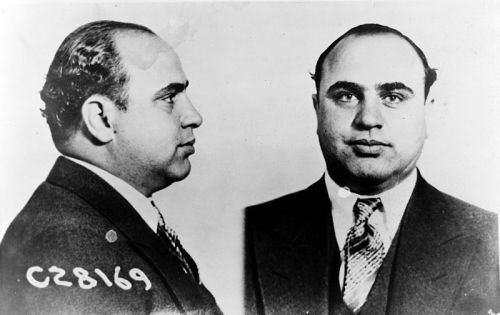 Mugshot of a man in a suit, showing profile and frontal views, with a number labeled on the side.